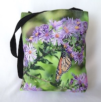 A tote bag with a photograph of an orange and black Monarch butterfly on purple aster flowers in front of green foliage.